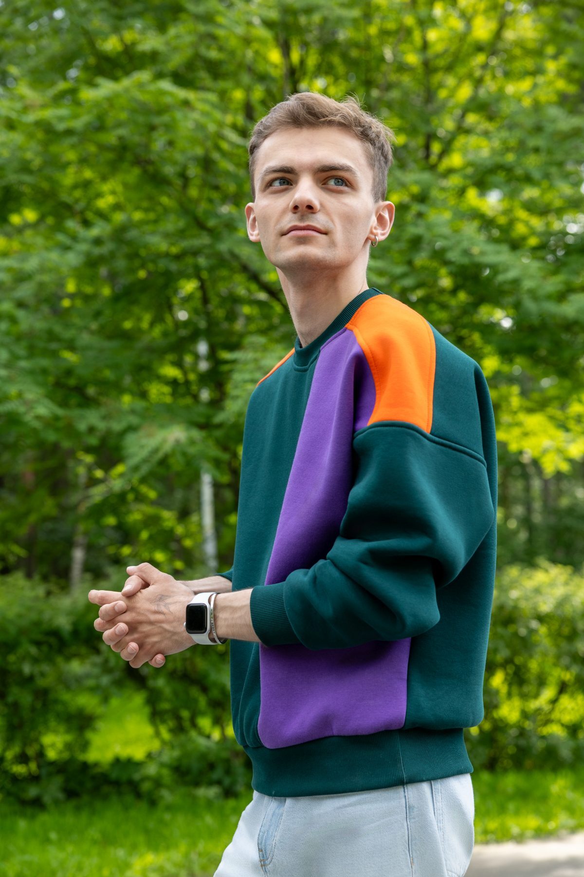 Side view of the colourblock sweatshirt worn against summer trees