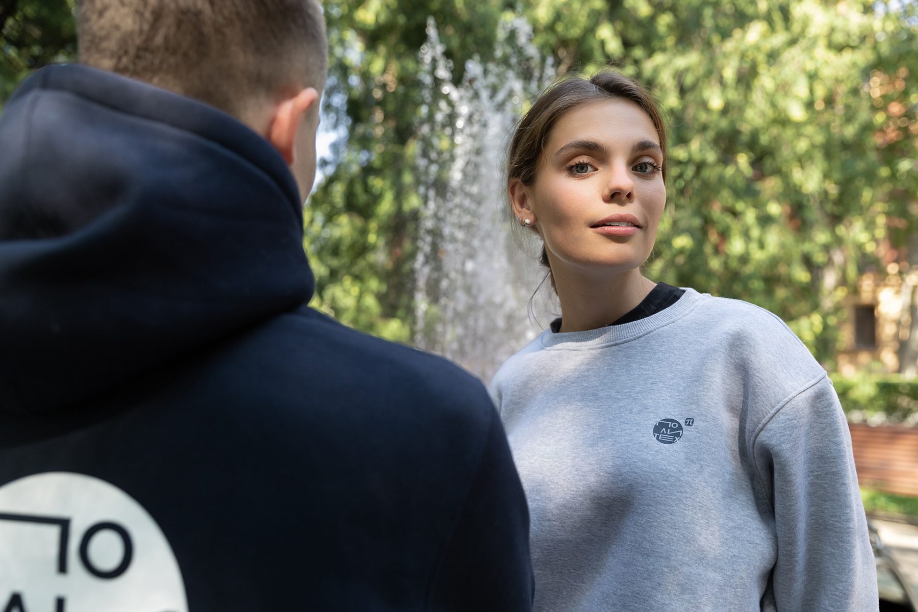 Grey embroidered crewneck and a navy hoodie back print by a fountain