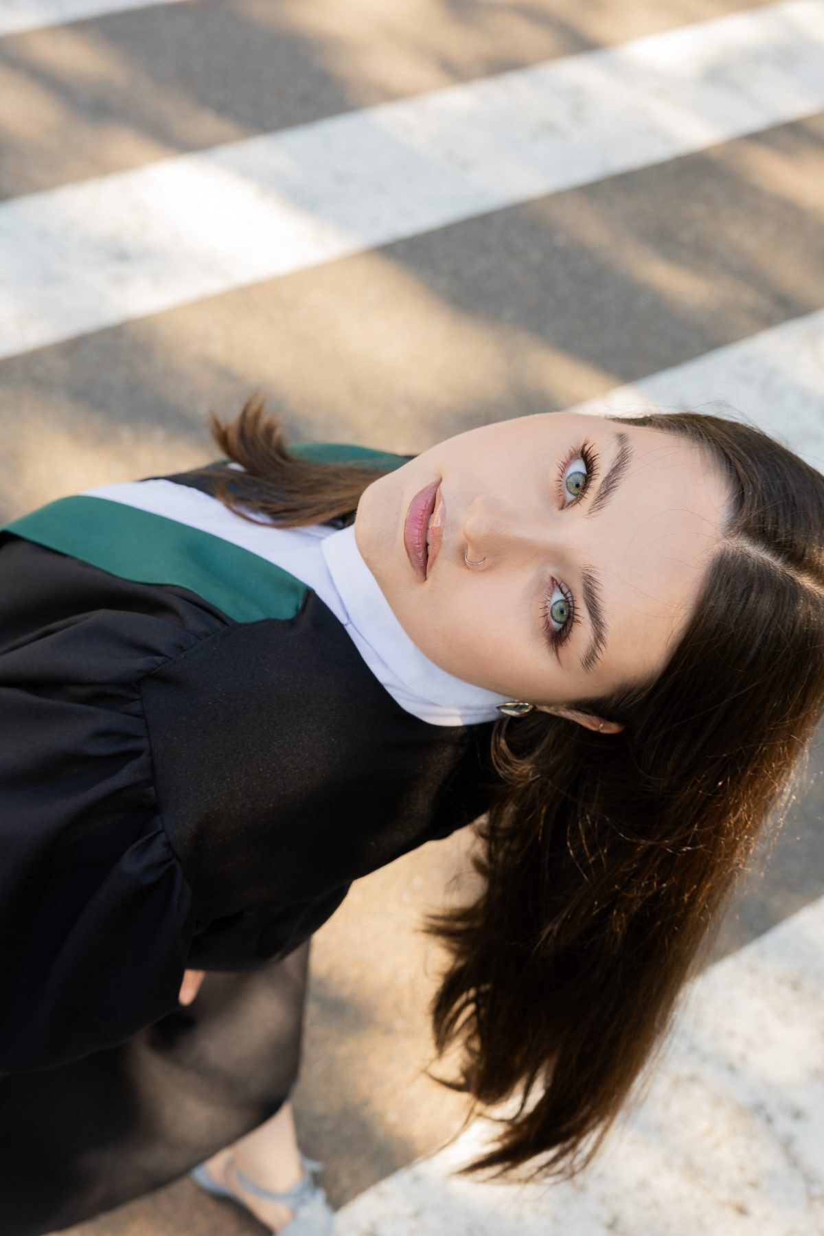 Overhead shot of a graduate in a green-trimmed robe standing on a crosswalk