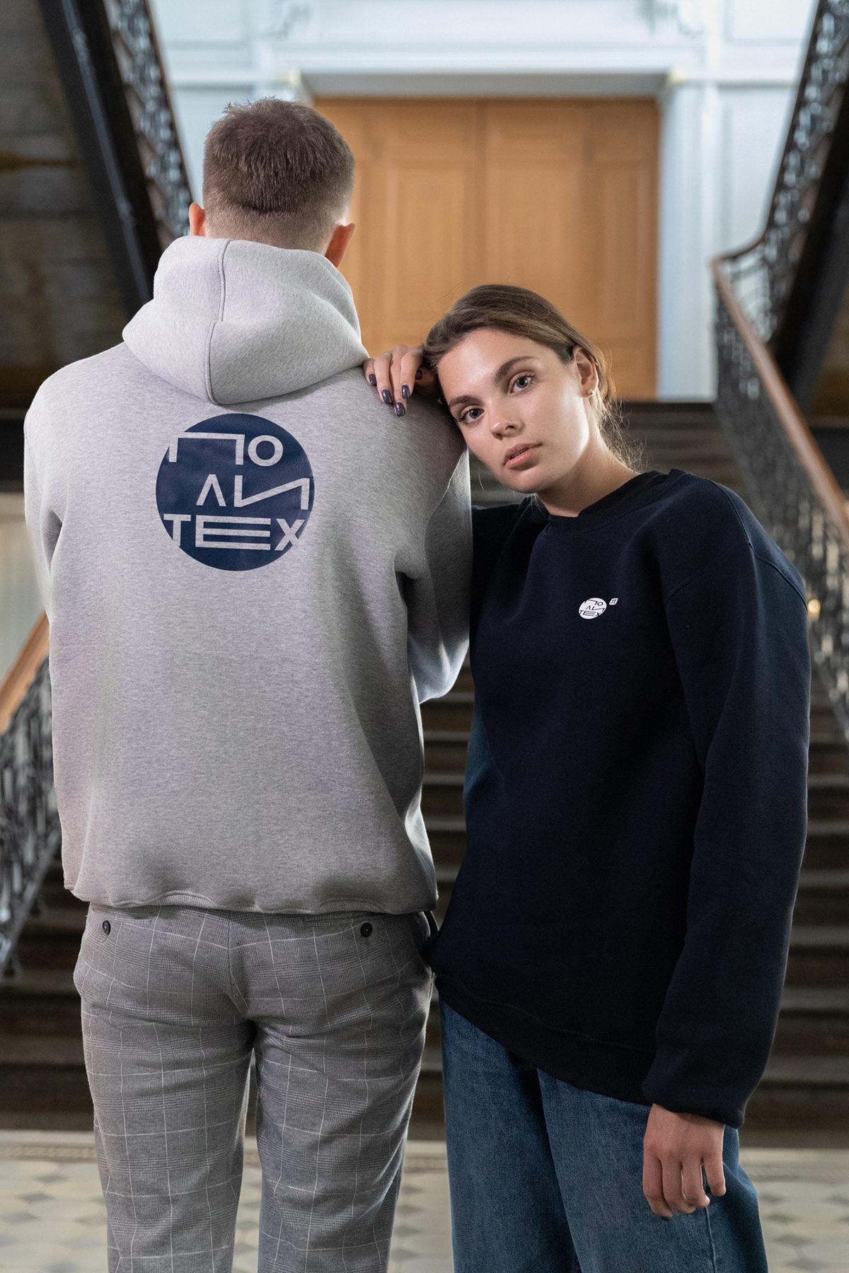 Grey hoodie with a large navy logo print on the back, next to a navy crewneck