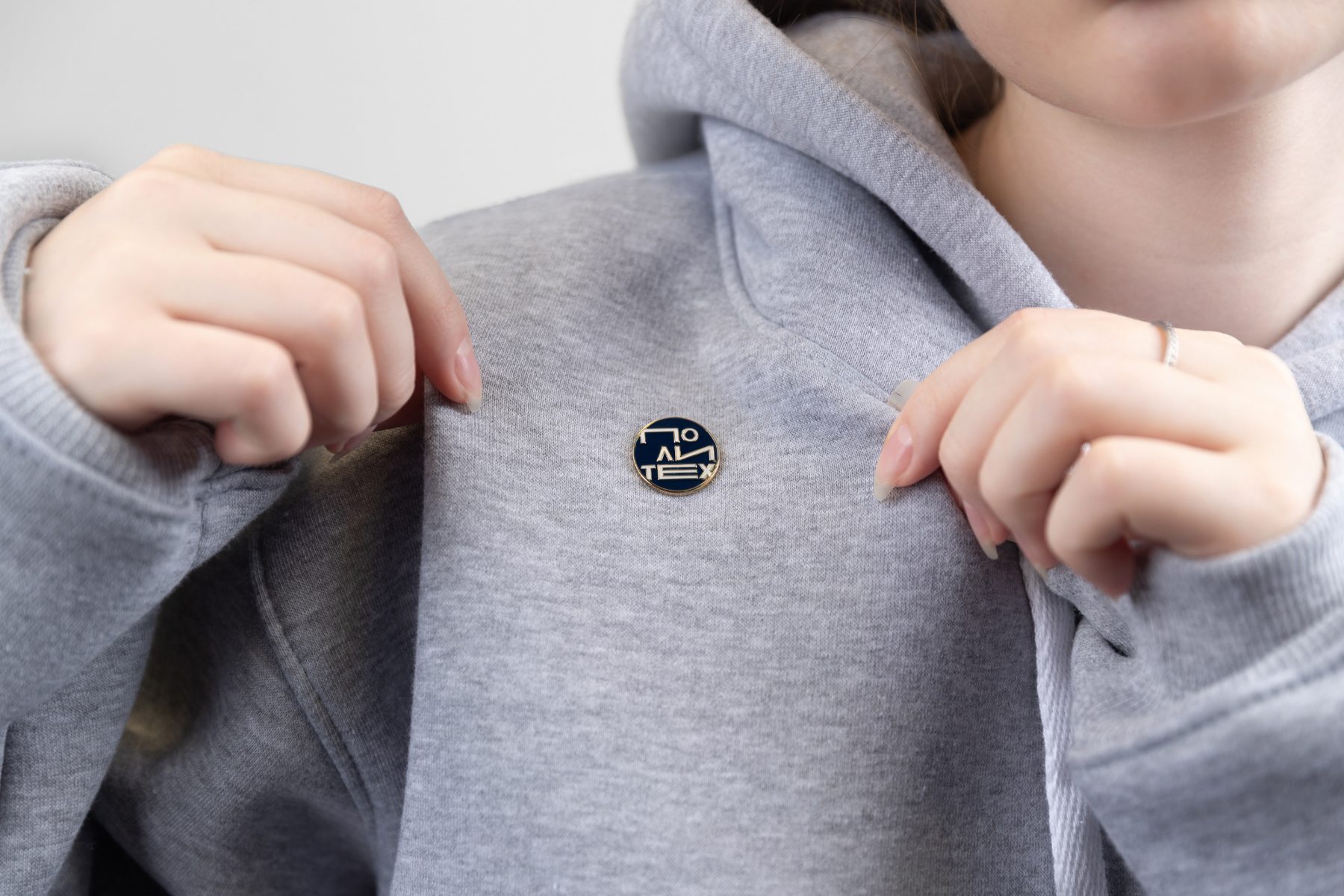 Close-up of a navy enamel logo pin on a grey hoodie