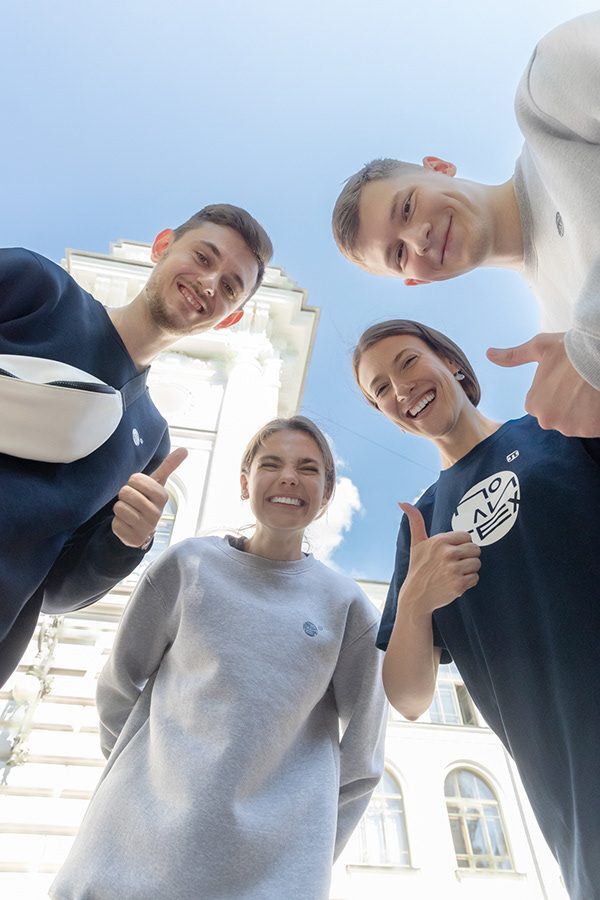 Four students in branded sweatshirts photographed from below against a bright sky