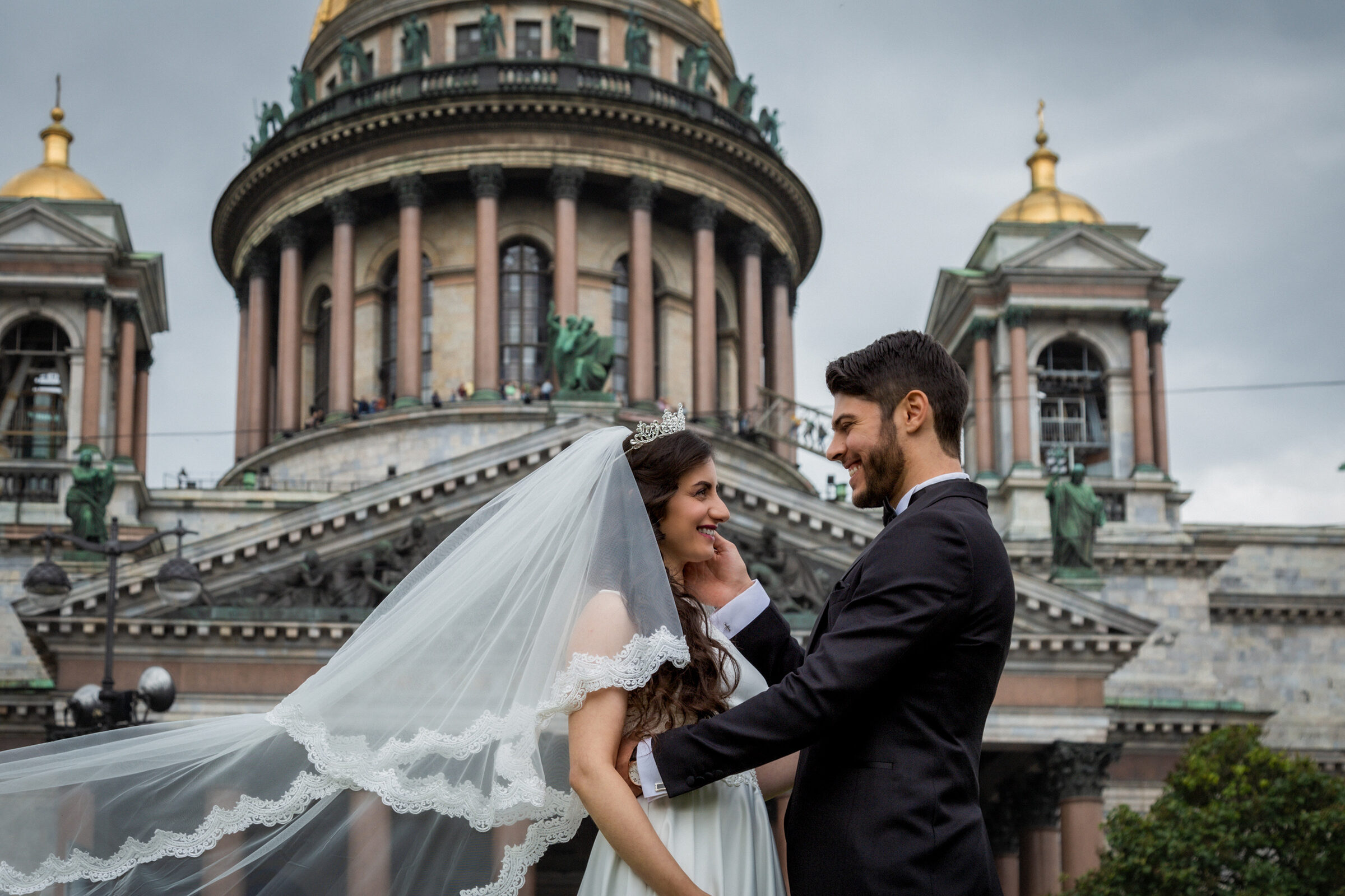 Groom touching the bride’s face as her veil blows out in front of St Isaac’s Cathedral
