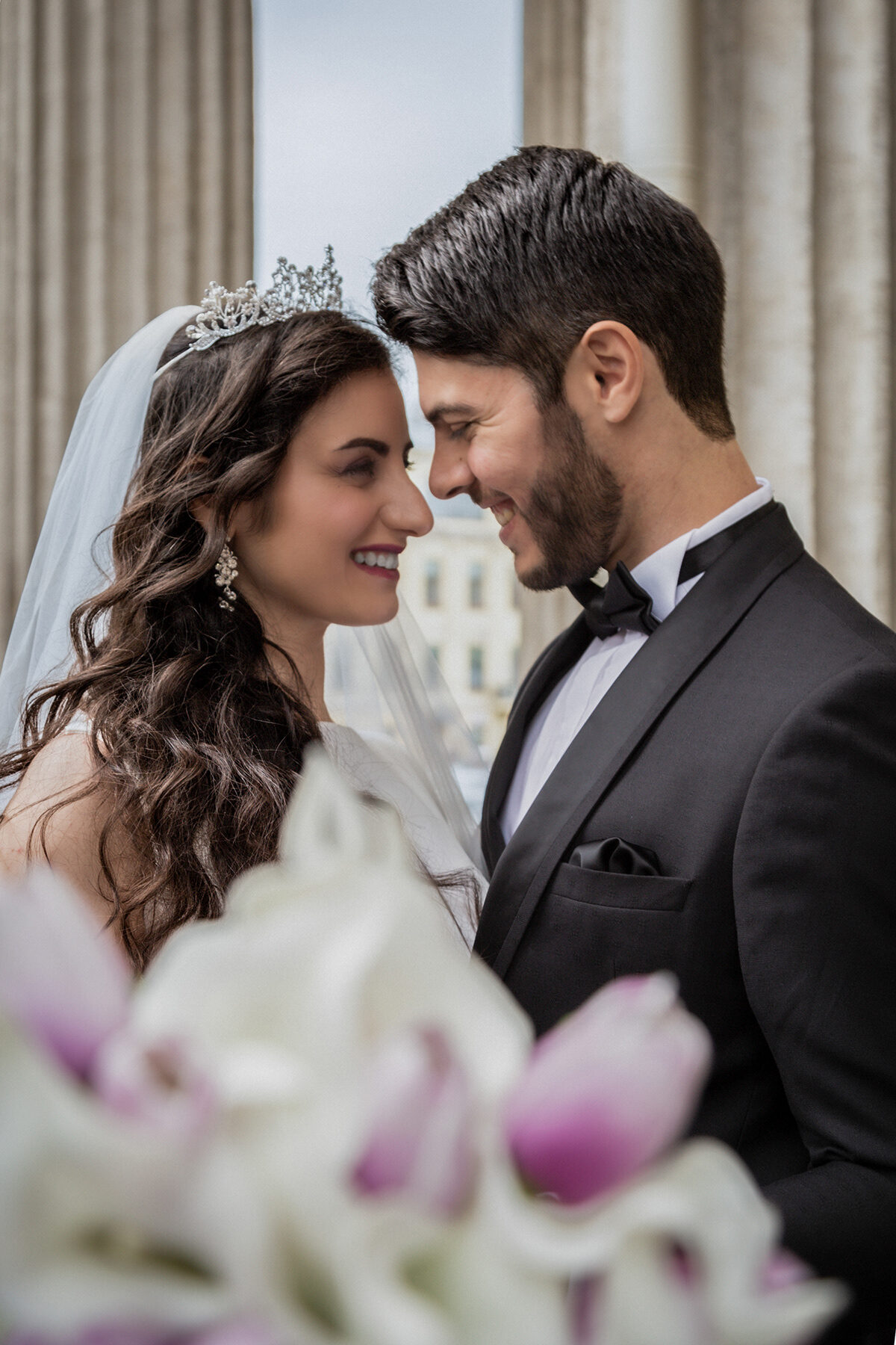 Close-up of the couple smiling nose to nose behind a blurred bouquet