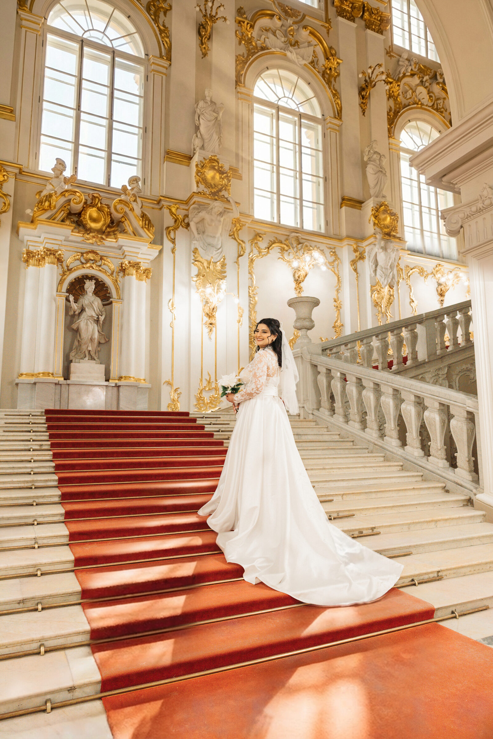 Bride looking back over her shoulder on a gilded staircase with a red carpet