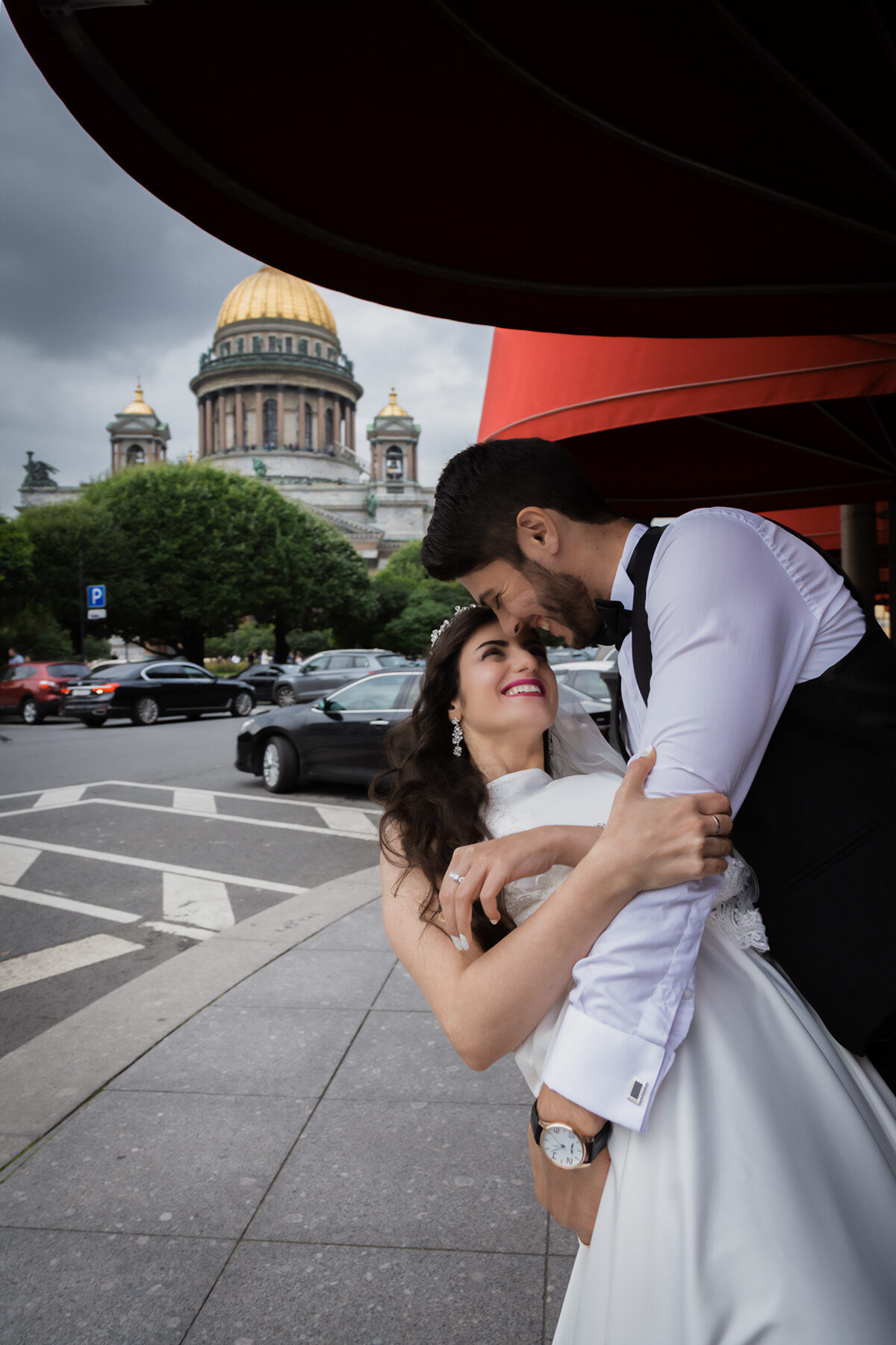 Bride laughing up at the groom under a red awning, the cathedral dome behind
