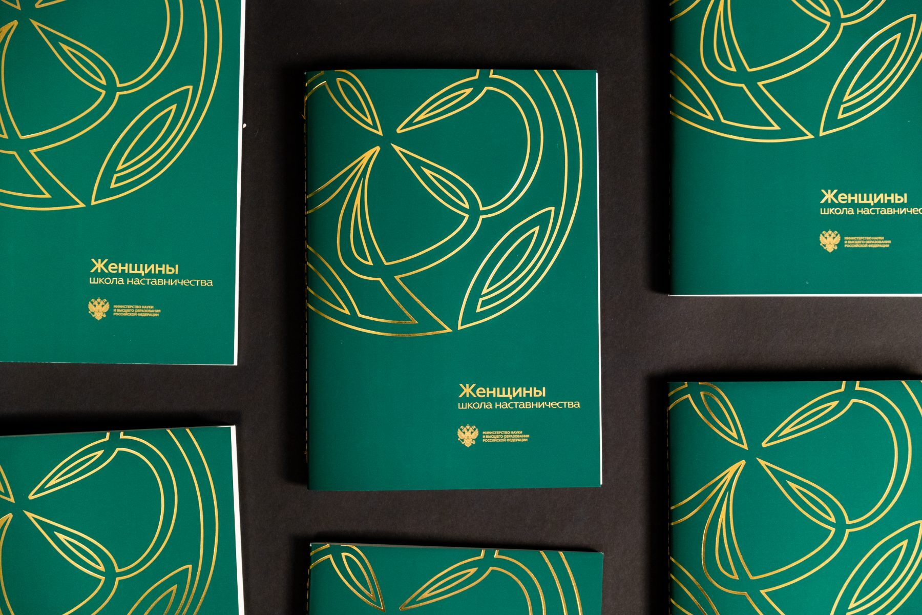 Several green foil-stamped booklets arranged in a grid on dark paper