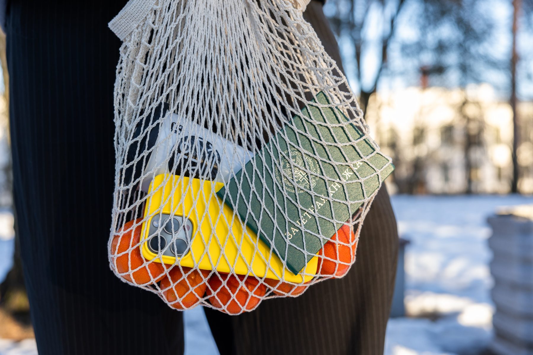 String bag holding mandarins, a yellow-cased phone and a green record book in winter sun