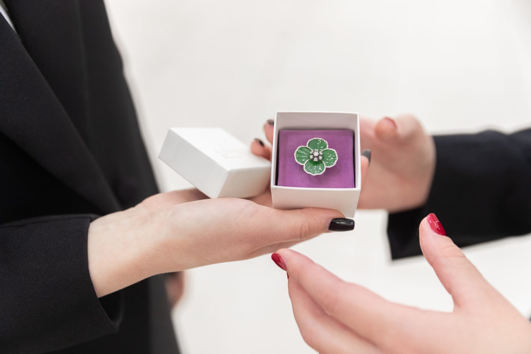 Hands presenting the boxed enamel flower pin to another pair of hands