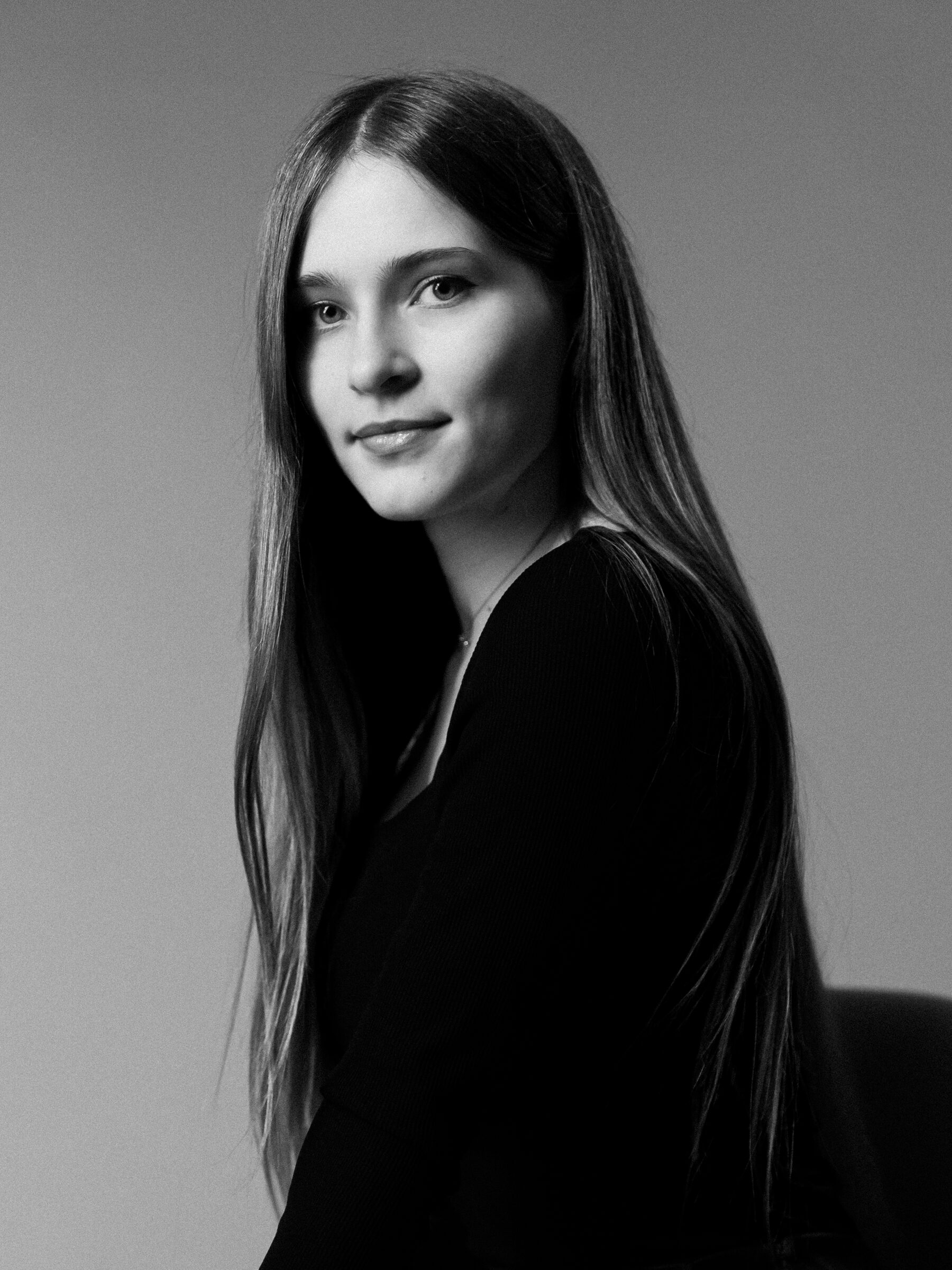 Black-and-white studio portrait of a woman with long straight hair in a black top