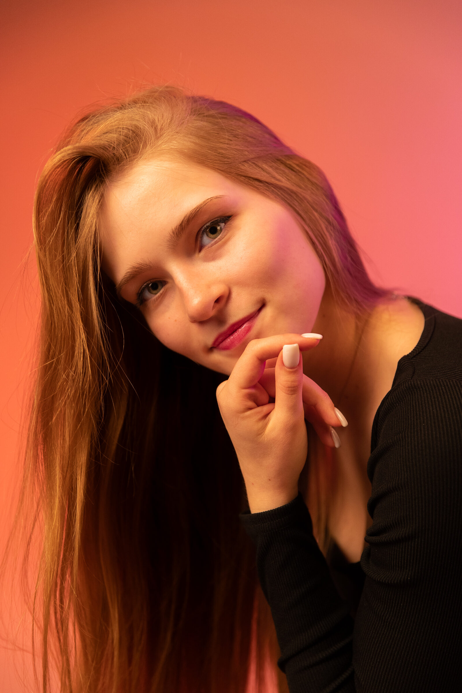 Woman resting her chin on her hand against a coral and pink gel-lit backdrop