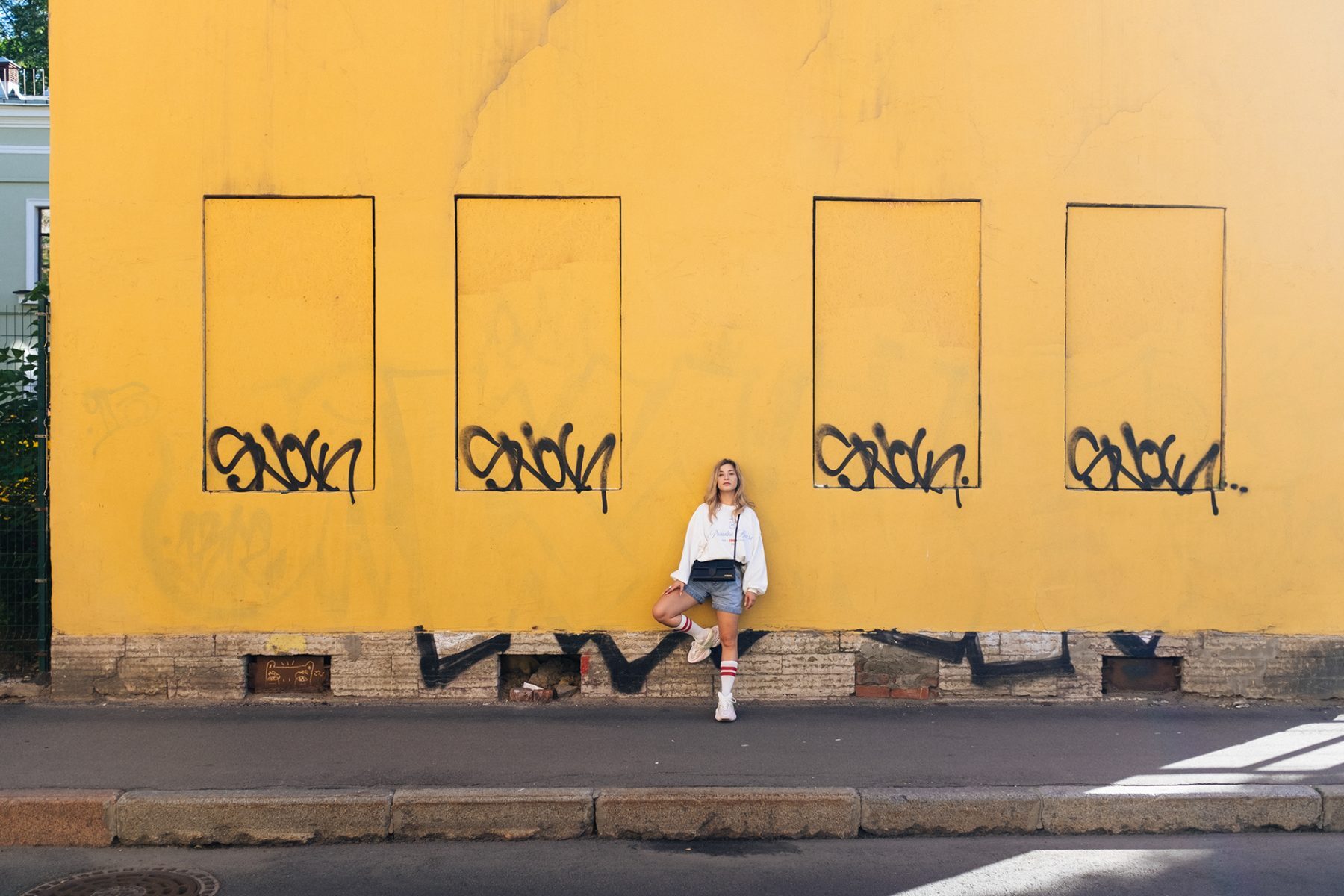 Wide portrait of a figure leaning against a large yellow wall with graffiti